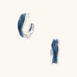 Silver huggie hoops with blue denim fabric inlay strip and polished white gold plated finish on cream background.