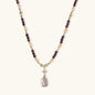 Gold necklace with iridescent baroque pearl pendant, purple amethyst beads, and crystal star charm on cream background