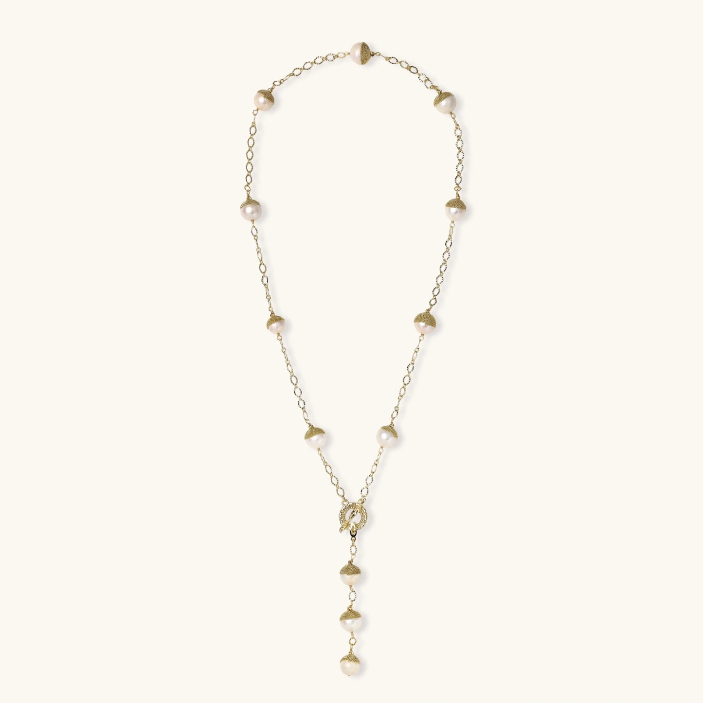 Gold-plated lariat necklace with baroque pearls and textured caps on cream background, showing adjustable Y-shaped design.