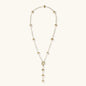 Gold-plated lariat necklace with baroque pearls and textured caps on cream background, showing adjustable Y-shaped design.
